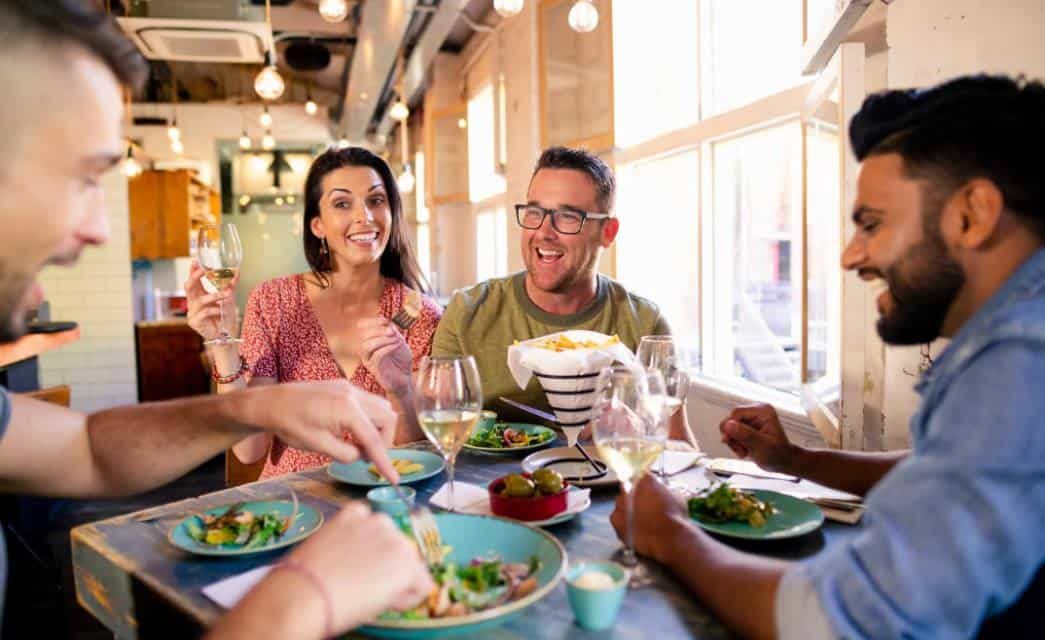 Two couples dining at a table underneath a large sunlit window